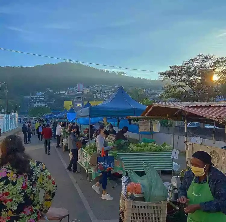 Pessoas circulando na feira, com vista para a Serra do Cristo.